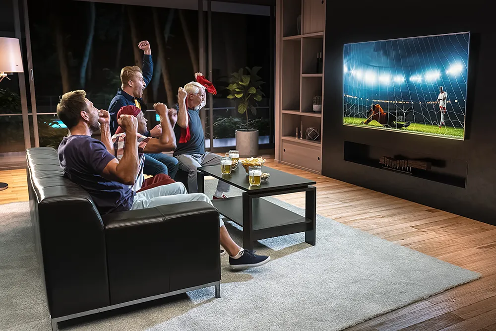 Eine Gruppe von Fans sieht sich einen Fußballmoment im Fernsehen an und feiert ein Tor, während sie auf der Couch im Wohnzimmer sitzen